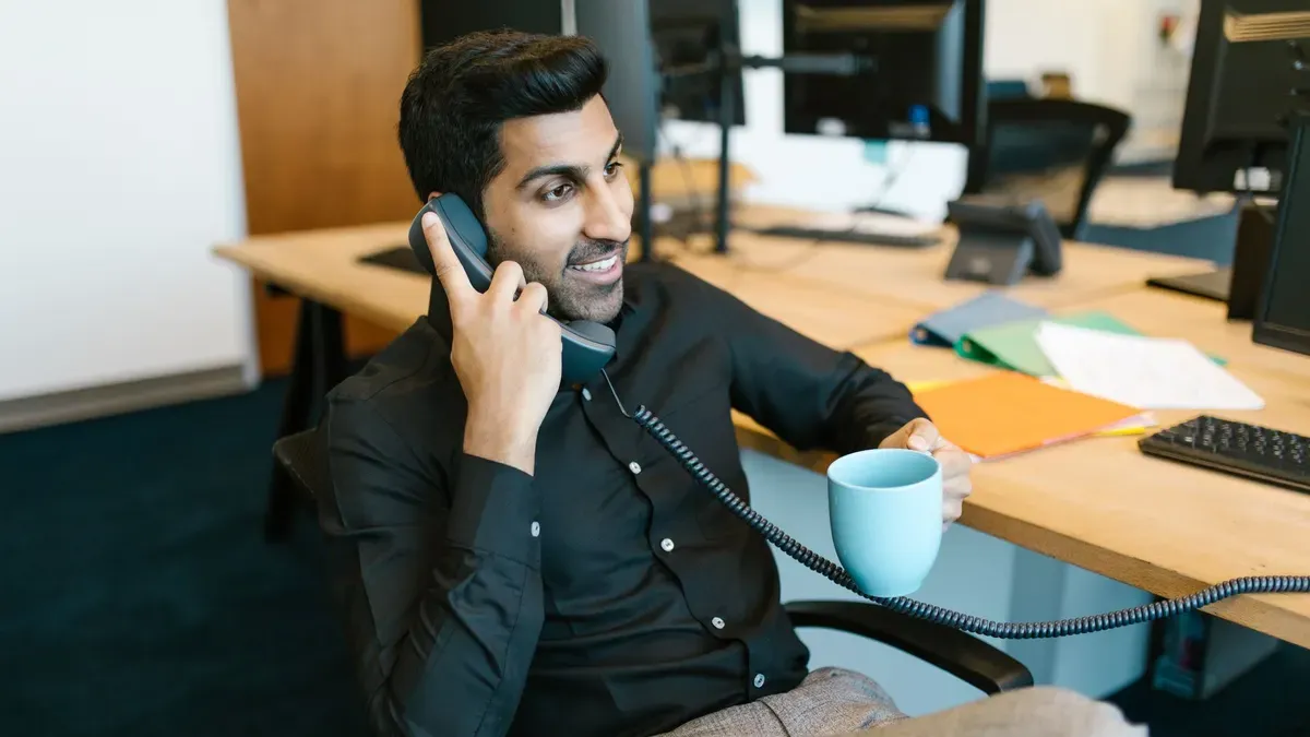 A smiling man on the phone at his desk, holding a mug