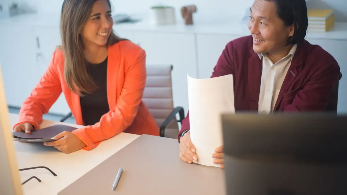 Two colleagues smiling while talking through documents in an office