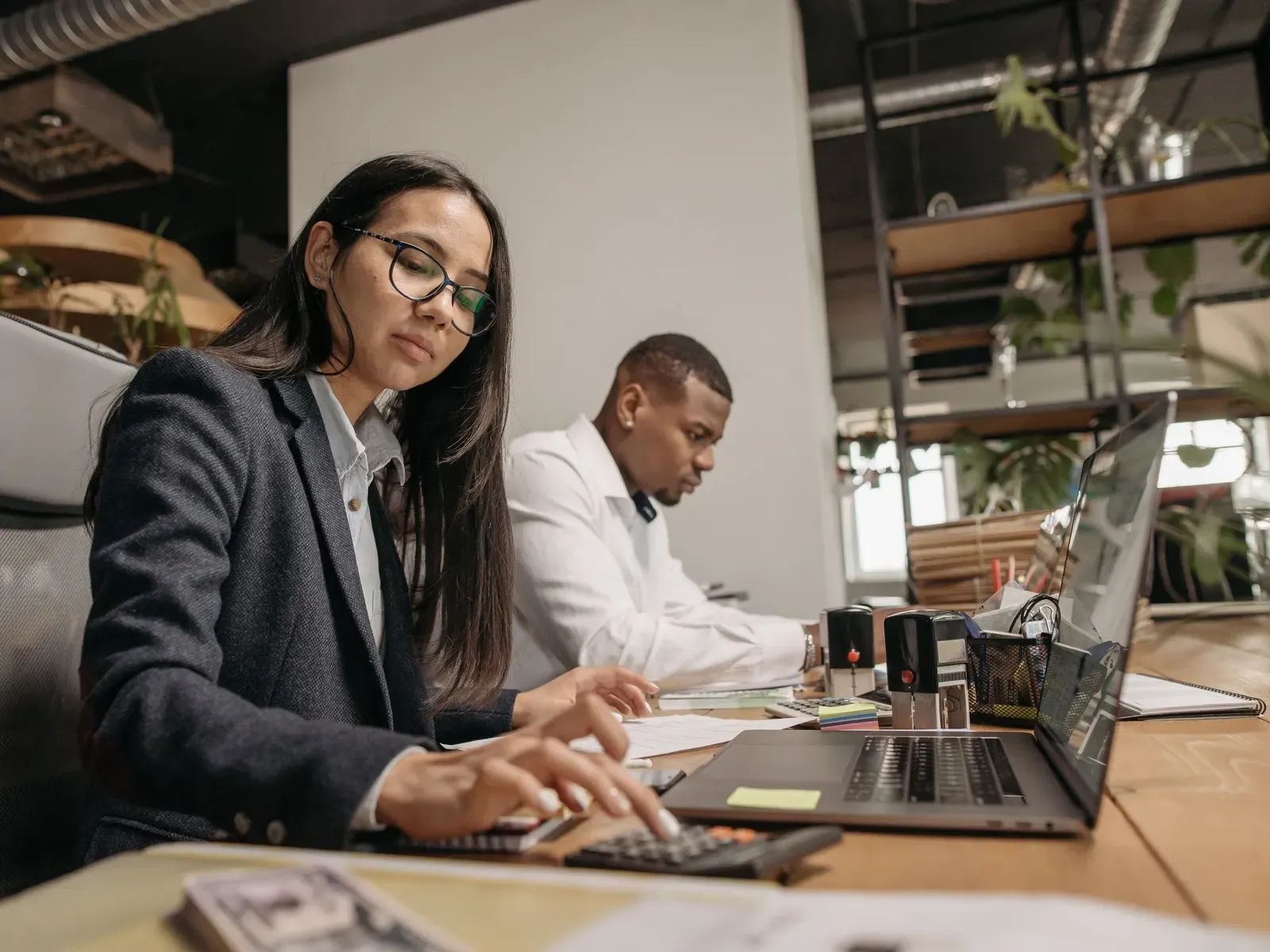 Two professionals working with laptops and calculators in a bright office